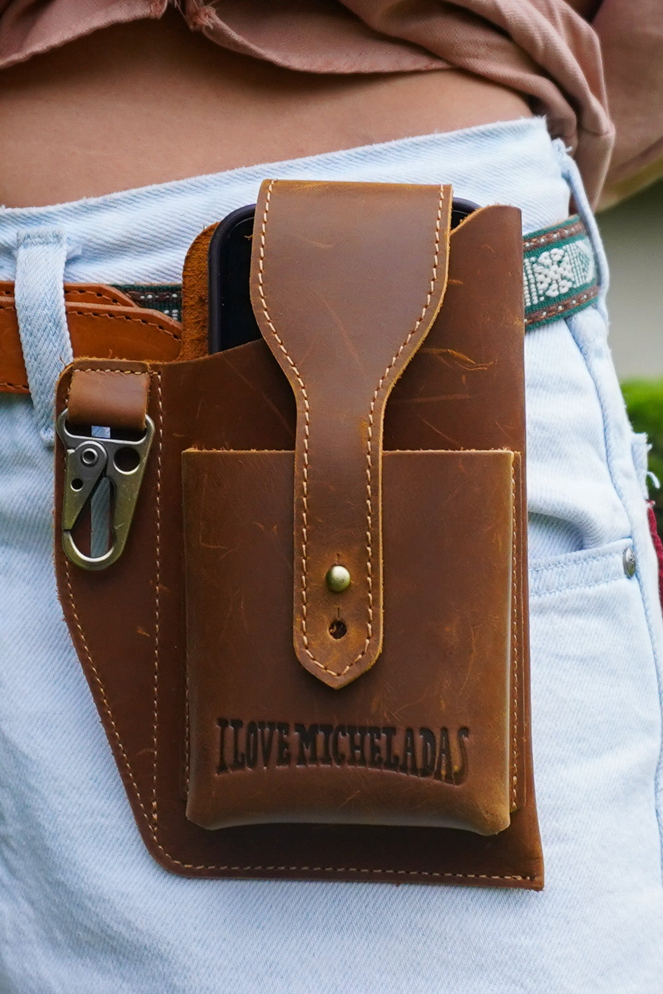 Brown leather phone holster with 'I Love Micheladas' text attached to a waistband.